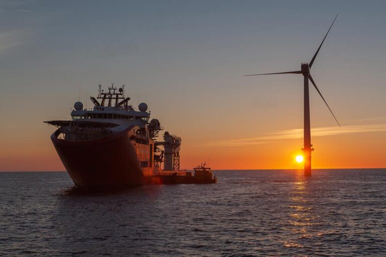 Offshore wind turbine at sunset, with service vessel in the foreground.