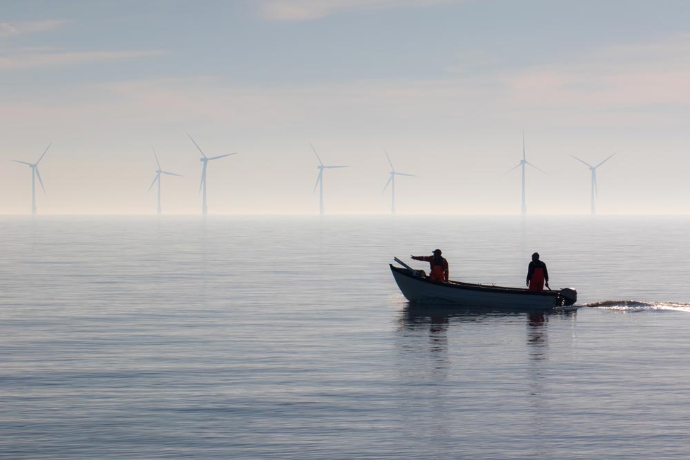 Small fishing boat with offshore wind turbines in the background.